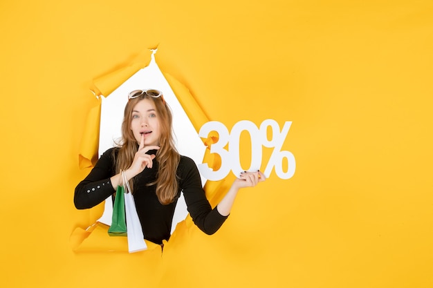 Young fashion woman holding shopping bags and discount percentage through torn paper hole in the wall