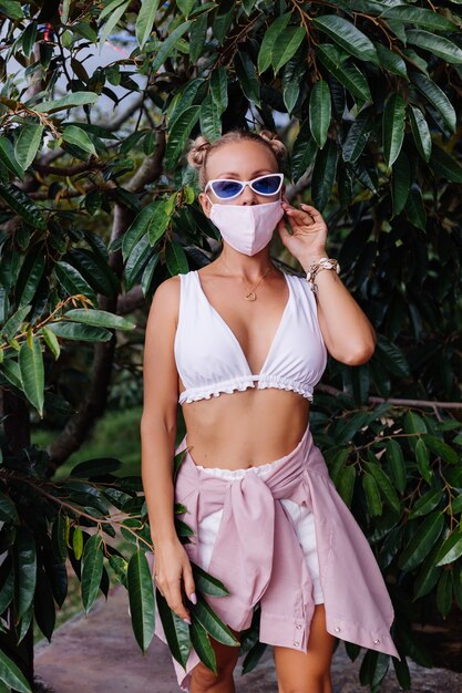 Young fashion woman in white crop top, sunglasses and white medical face mask in the nature