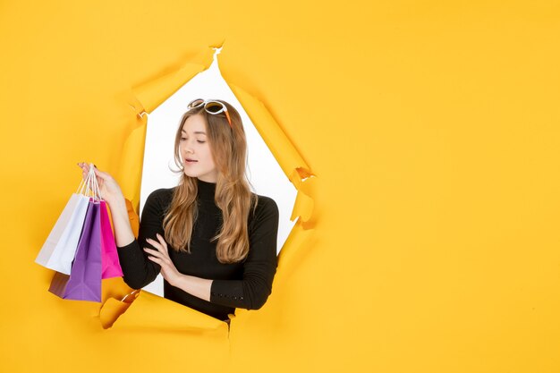 Young fashion woman with shopping bags through torn paper hole in the wall