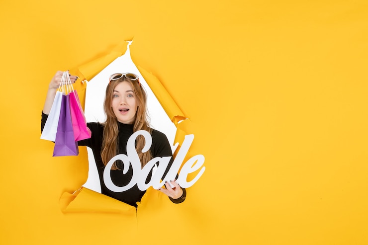 Free Photo young fashion woman with shopping bags through torn paper hole in the wall