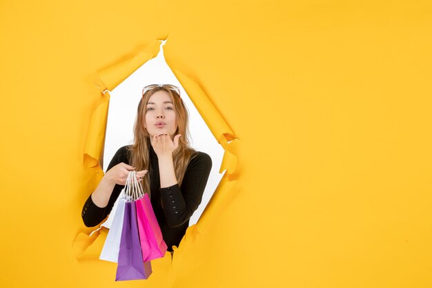 Young fashion woman with shopping bags through torn paper hole in the wall