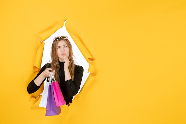 Young fashion woman with shopping bags through torn paper hole in the wall