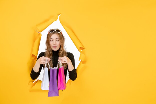 Young fashion woman with shopping bags through torn paper hole in the wall