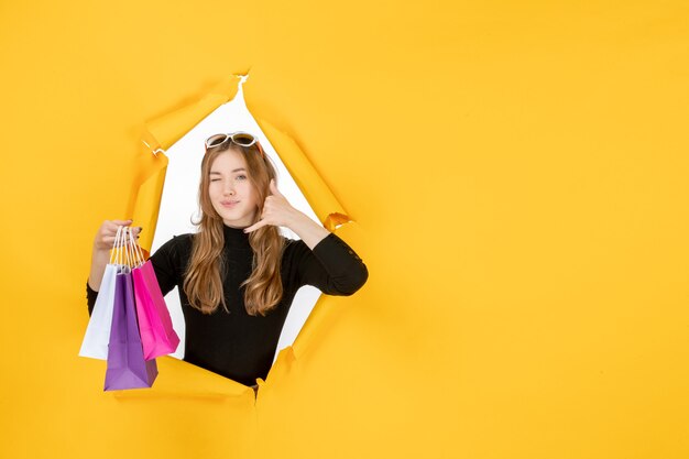 Молодая модная женщина с хозяйственными сумками через рваную бумажную дыру в стене