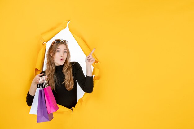 Young fashion woman with shopping bags through torn paper hole in the wall