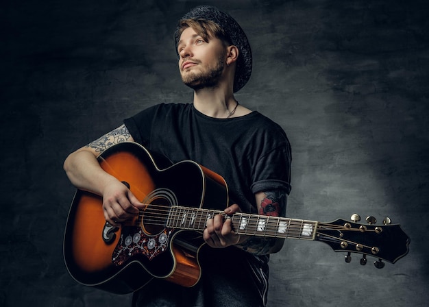 Young fashionable hipster blues and jazz acoustic guitar player with tattoos on his arms playing melody.