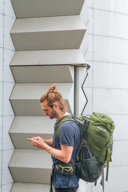 Young fashionable male traveler carrying backpack using cellphone at outdoors