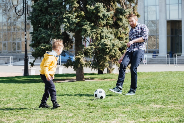 Молодой отец и его сын играют в футбол в парке