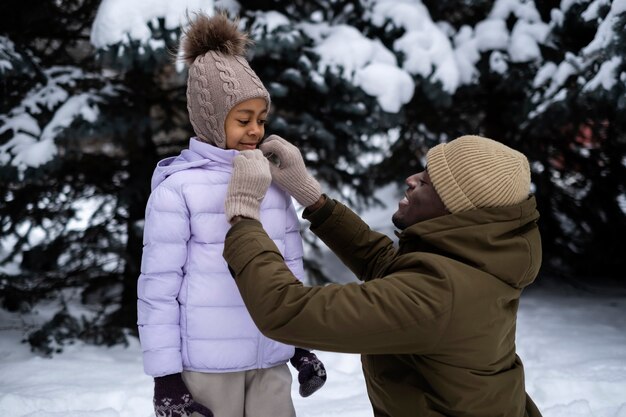 Free photo young father tying his daughter's jacked on a snowy winter day