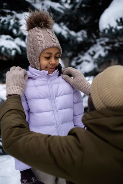 Free photo young father tying his daughter's jacked on a snowy winter day