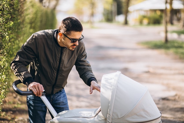 Free photo young father walking with baby carriage in the park