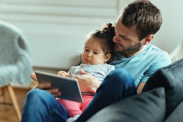 Young father with small daughter watching something on digital tablet at home