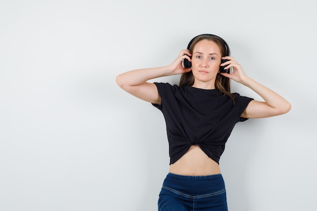 Foto gratuita giovani cuffie di regolazione femminile in camicetta nera, pantaloni e un bell'aspetto