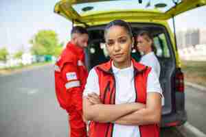 Free photo young female african american paramedic standing rear of the ambulance paramedics by the ambulance two paramedics taking out strecher from ambulance