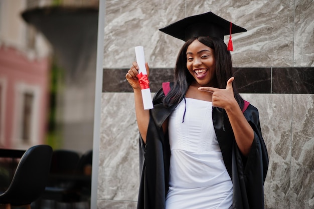 卒業証書を持つ若い女性のアフリカ系アメリカ人の学生が屋外でポーズをとるxA