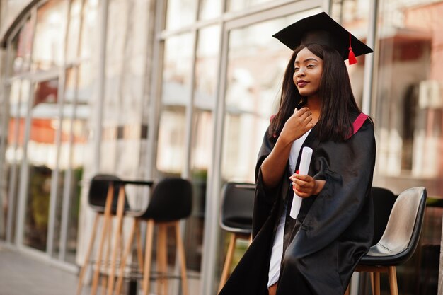 卒業証書を持つ若い女性のアフリカ系アメリカ人の学生が屋外でポーズをとるxA