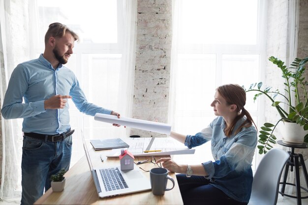 Young female architecture giving blueprint to her colleagues at office