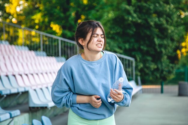 A young female athlete drinking water after training pain in her side