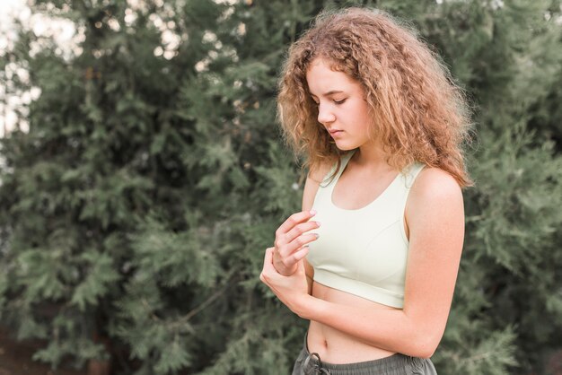 Young female athlete having wrist pain standing against tree