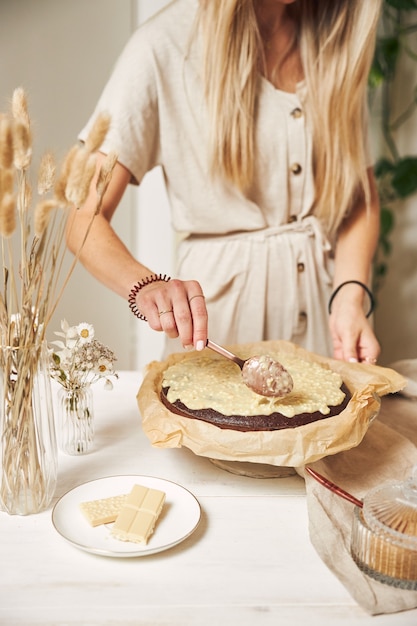 하얀 탁자에 크림을 얹은 맛있는 초콜릿 케이크를 만드는 젊은 여성 제빵사