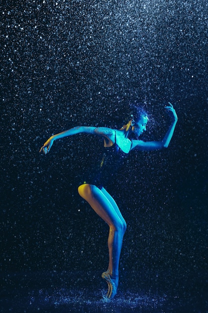 Молодая артистка балета исполняет под каплями воды и брызгами. Кавказская модель танцует в неоновых огнях. Привлекательная женщина. Концепция балета и современной хореографии. Творческое художественное фото.