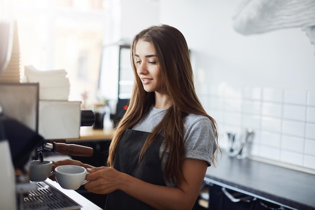 Бесплатное фото Молодая женщина-бариста готовит кофе по утрам. успешный бизнес требует самоотверженности.