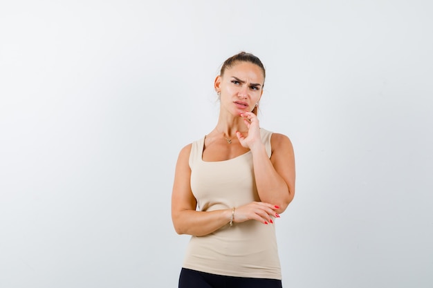 Young female in beige tank top standing in thinking pose and looking pensive