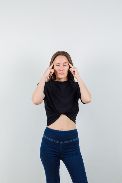 Young female in black blouse, pants holding fingers on temples and looking fatigued