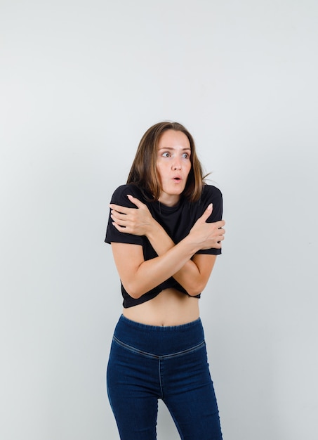 Young female in black blouse, pants hugging herself and feeling cold