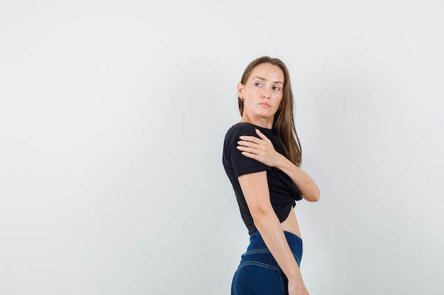 Giovane donna in camicetta nera, pantaloni guardando indietro con la mano sull'altro braccio e guardando seria