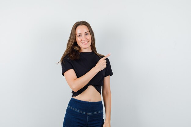 Young female in black blouse, pants pointing away and looking happy