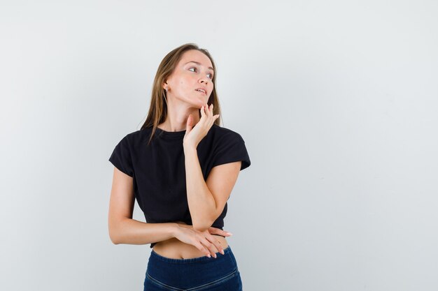 Young female in black blouse, pants posing while looking away and looking striking