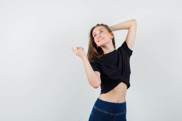 Free photo young female in black blouse, pants posing while pointing away and looking cheery