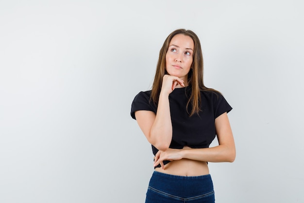 Giovane donna in camicetta nera, pantaloni appoggiando il mento a portata di mano e guardando pensieroso