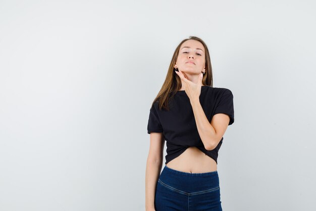 Young female in black blouse, pants touching neck and looking alluring