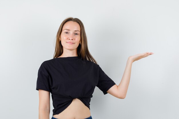 Young female in black blouse raising palm like holding something and looking confident