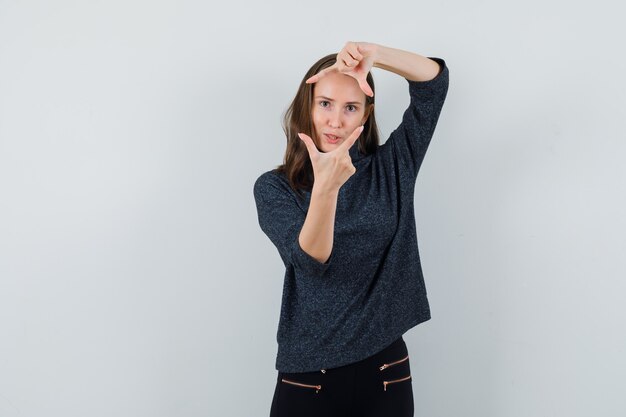 Young female in black blouse showing frame gesture and looking concentrated 