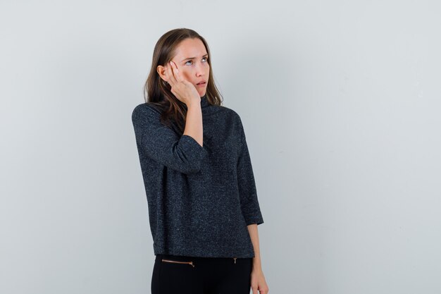 Young female in black blouse touching her temple and looking weird 