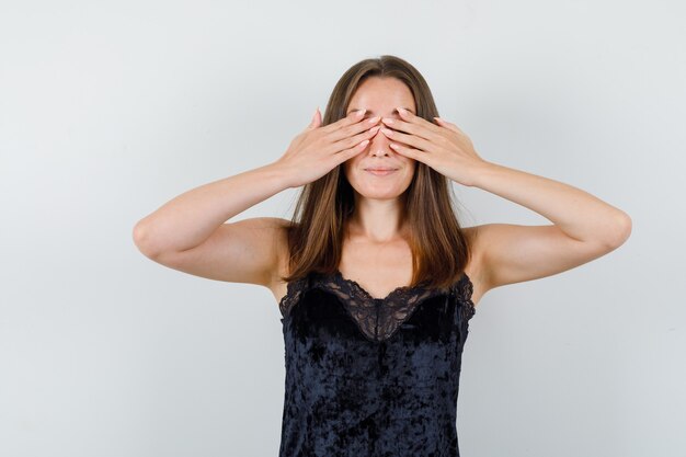 Young female in black singlet covering eyes with hands and looking excited