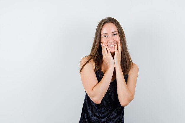 Young female in black singlet holding hands on cheeks and looking joyful