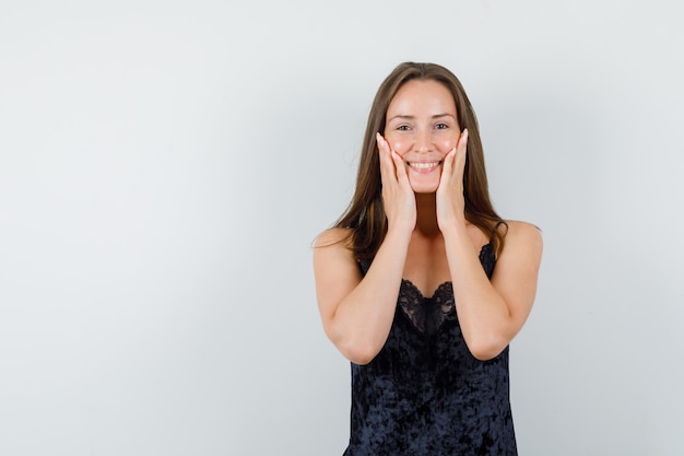 Young female in black singlet holding hands on cheeks and looking pretty