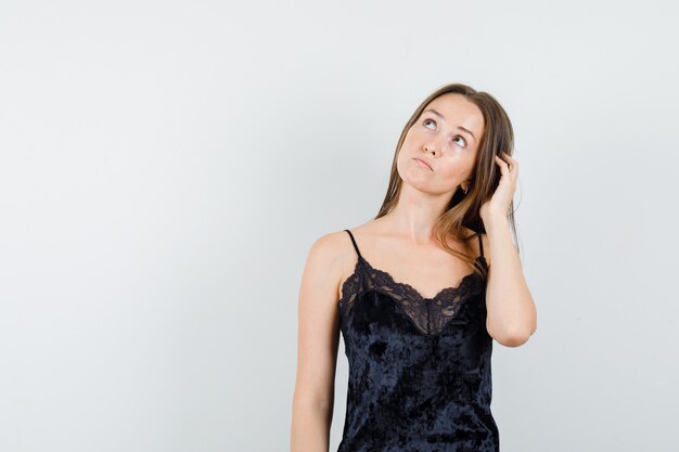 Young female in black singlet looking up while scratching head and looking pensive