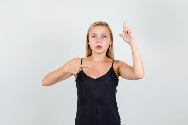 Free photo young female in black singlet pointing fingers with gun gesture and looking serious