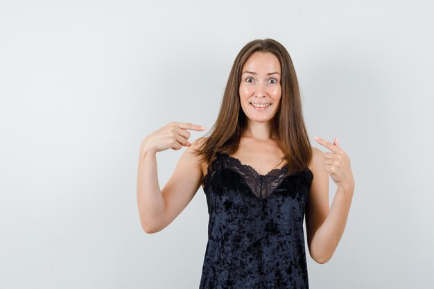 Young female in black singlet pointing at herself to ask 'me?' and looking surprised