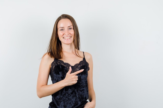 Young female in black singlet pointing to side and looking jolly