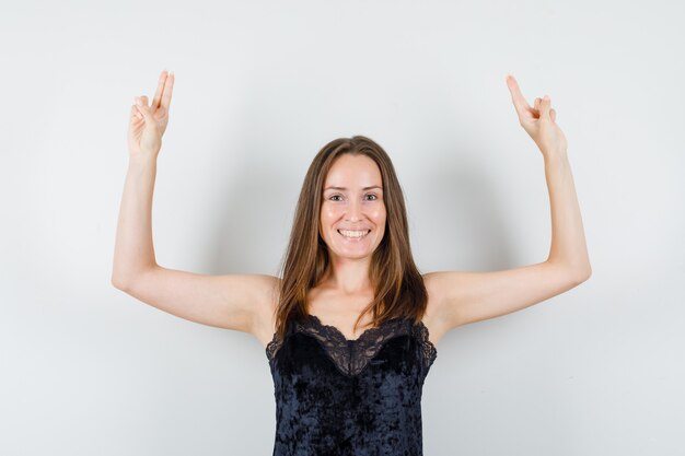 Young female in black singlet raising arms with two fingers and looking cheerful
