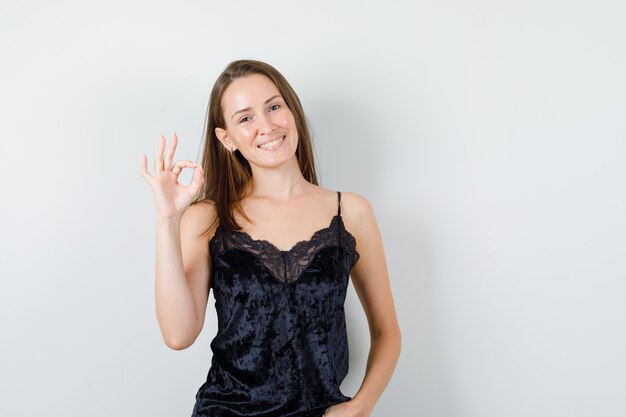 Young female in black singlet showing ok gesture and looking merry