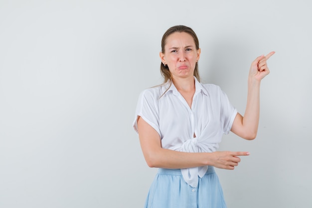 Young female in blouse, skirt pointing aside and looking offended