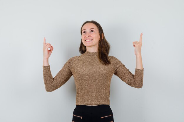 Young female in blouse,skirt pointing up and looking glad , front view.