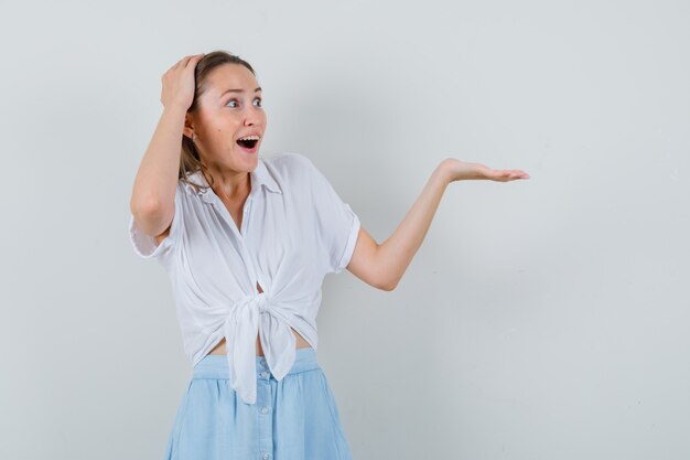 Young female in blouse and skirt spreading palm aside and looking happy